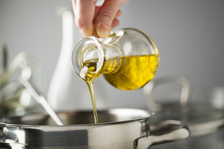 Pouring high-quality olive oil into a stainless steel pot for healthy cooking.