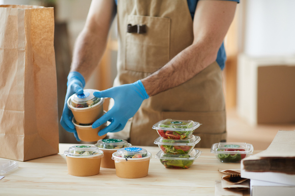 Worker in gloves preparing healthy meals for delivery in a clean kitchen space.