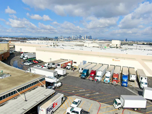 Busy logistics hub with delivery trucks and warehouses under a partly cloudy sky.